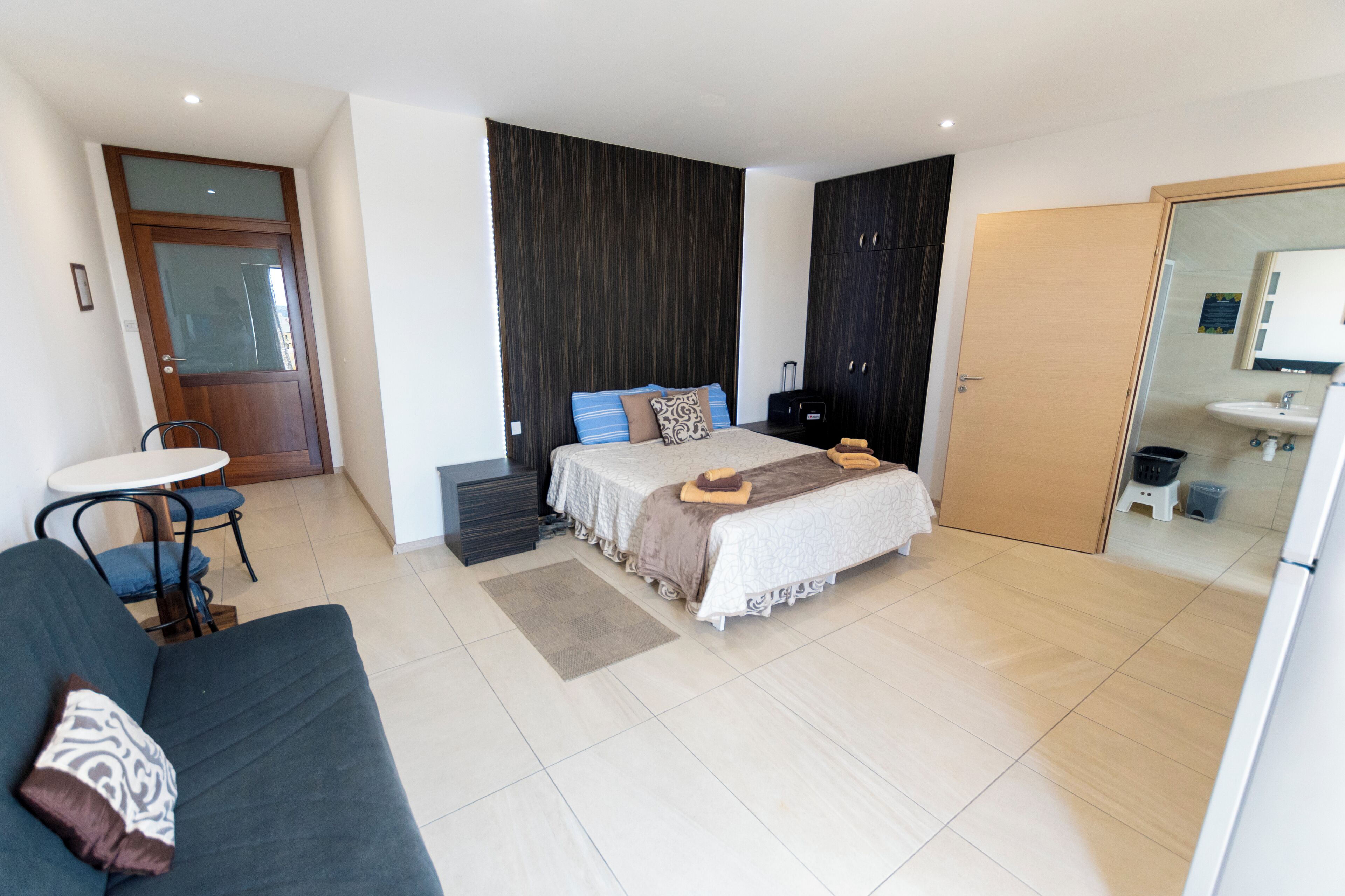 A modern hotel room with a bed, a small table, a sofa, a wardrobe, and a bathroom.