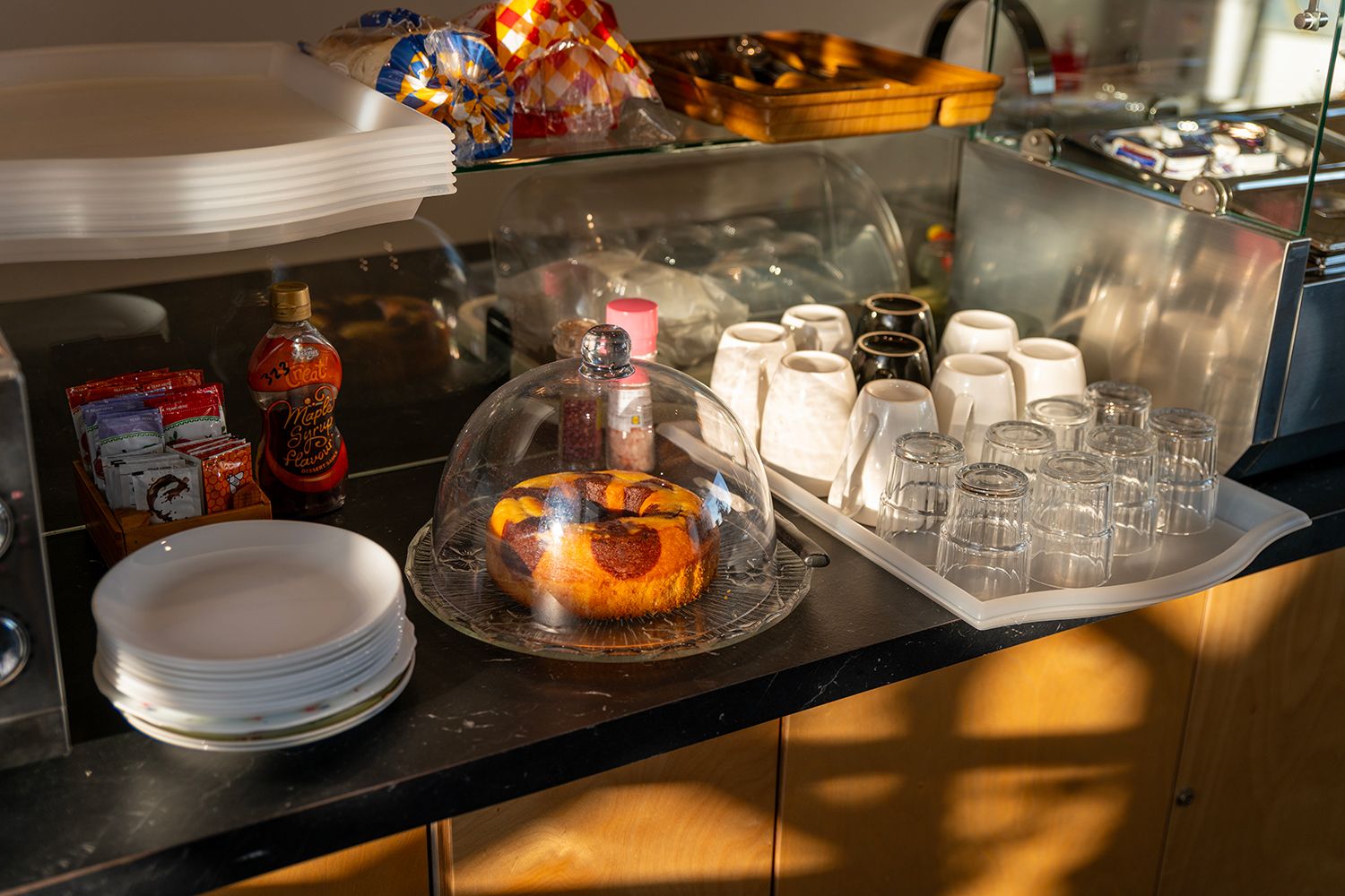 Montaje de bufé con un pastel cubierto, botellas de condimentos y platos apilados.