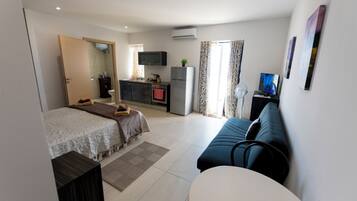 Una habitación de hotel moderna con cama, sofá, una mesita, televisión y kitchenette.