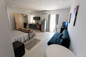 A modern hotel room with a bed, a sofa, a small table, a TV, and a kitchenette. - Estrella Lodging (Rabat)