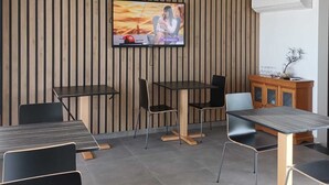 Ein modernes Interieur mit an einer Holzwand montiertem Fernseher, einem Holzschrank mit Gläsern und einer Sitzecke mit Tischen und Stühlen.
