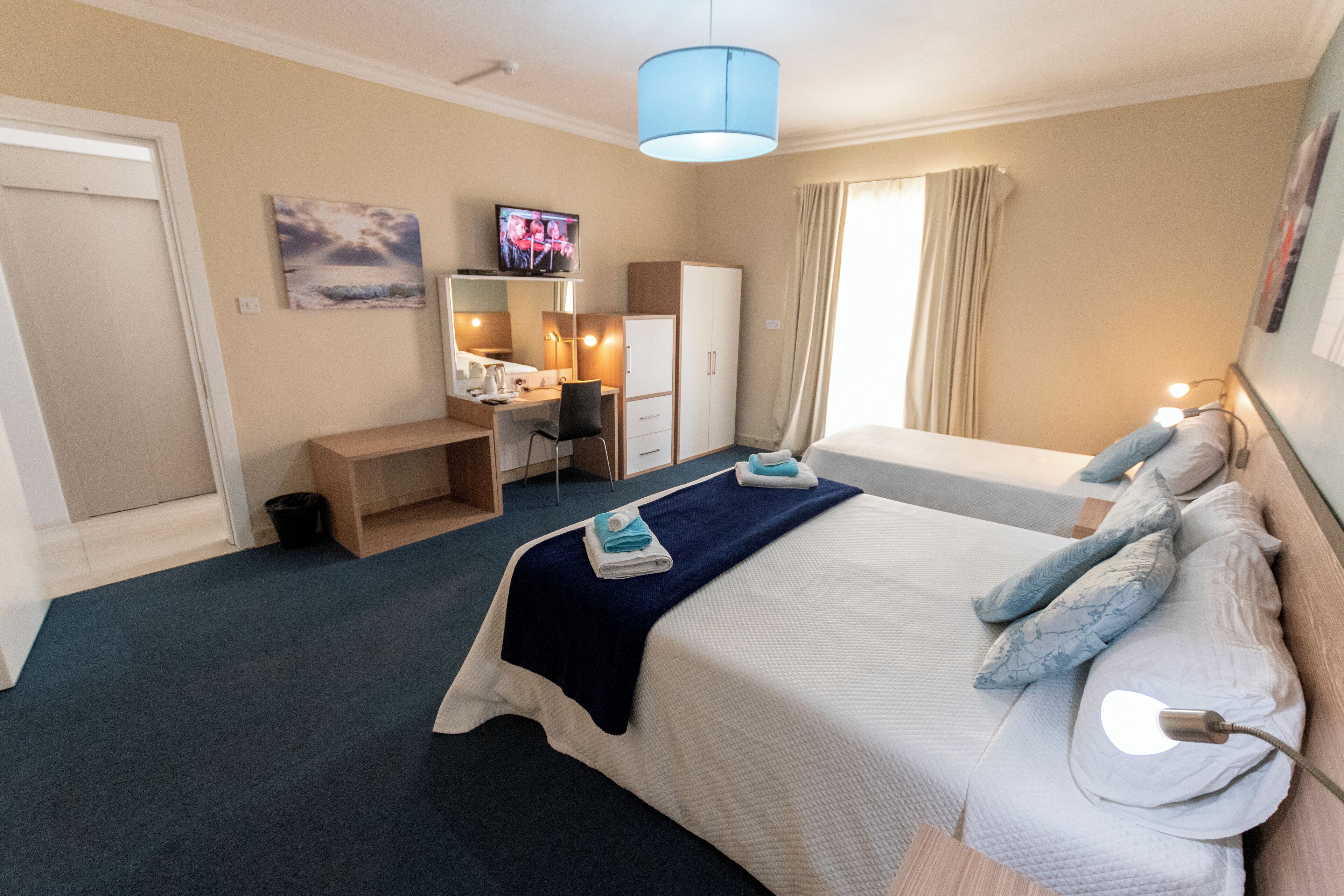 A hotel room with a bed, a desk, a chair, a television, and a wardrobe.
