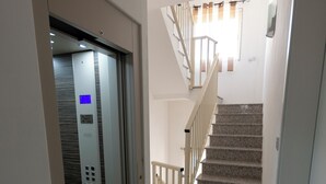 Ein modernes Interieur mit einem Glaselevator, einer Treppe mit Holelllaufgeländern und einer Tür mit Griff.