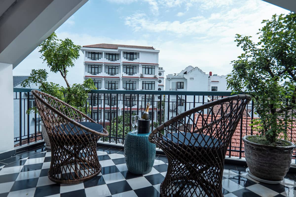 A balcony with checkered flooring, wicker chairs, and potted plants.