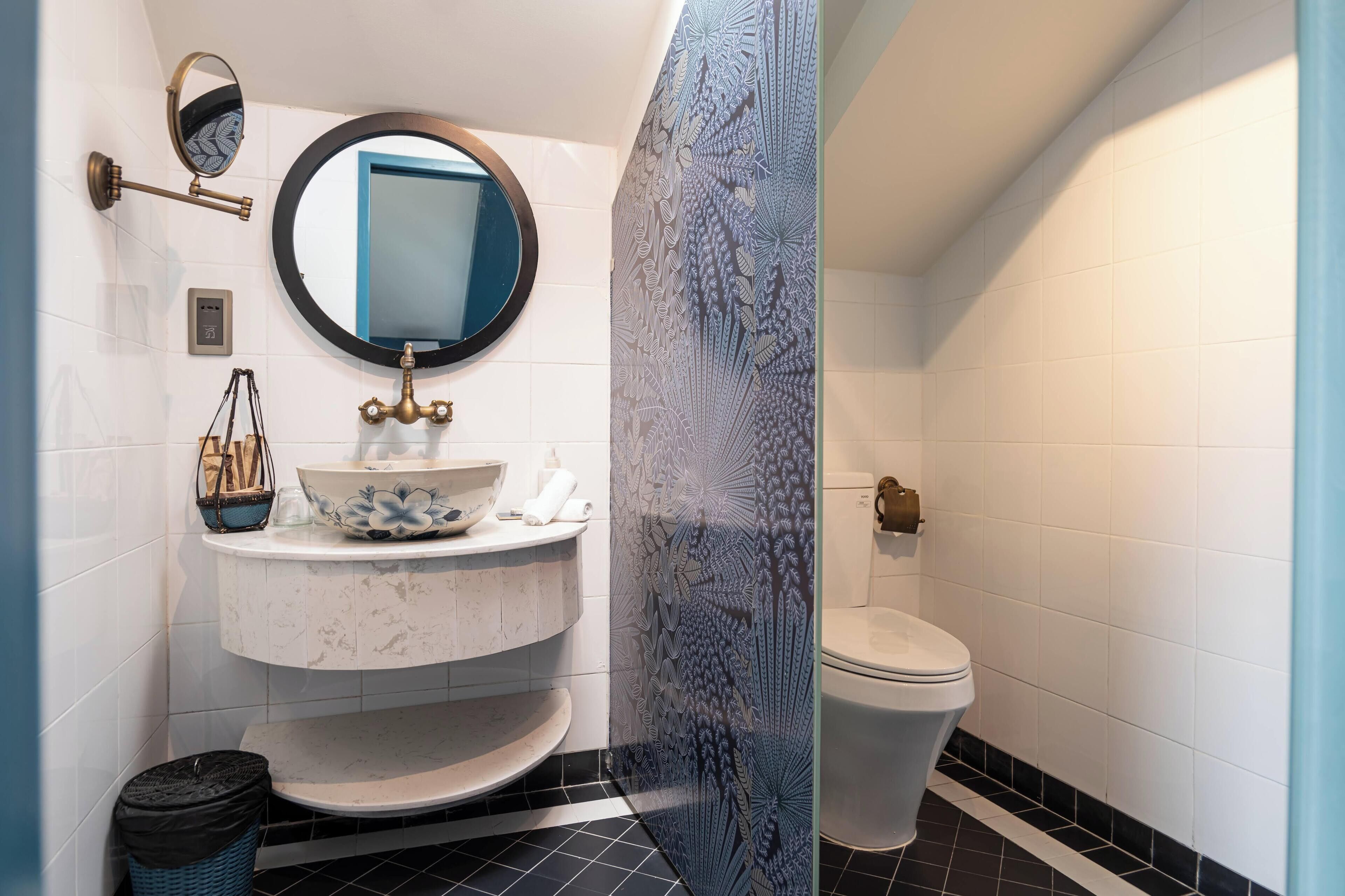 A bathroom with a white sink, a round mirror, a toilet, and a patterned shower door.
