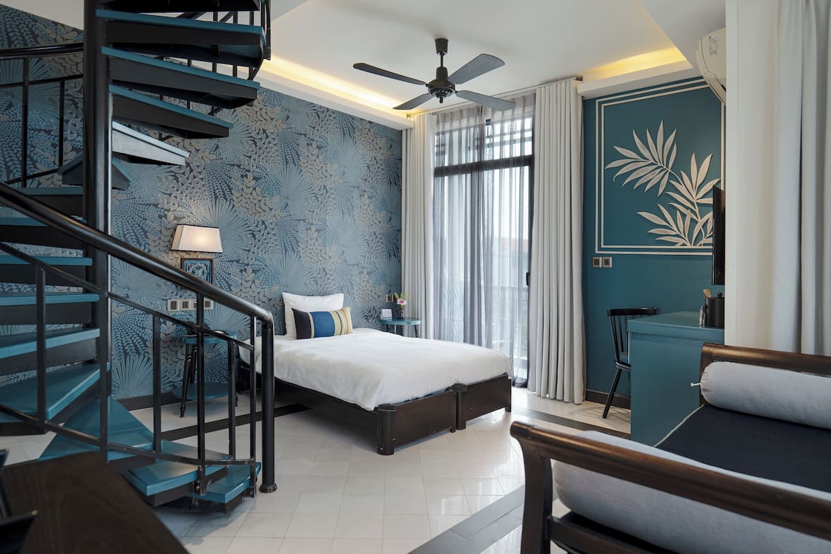 A bedroom with a bed, a desk, a chair, a ceiling fan, and a staircase.