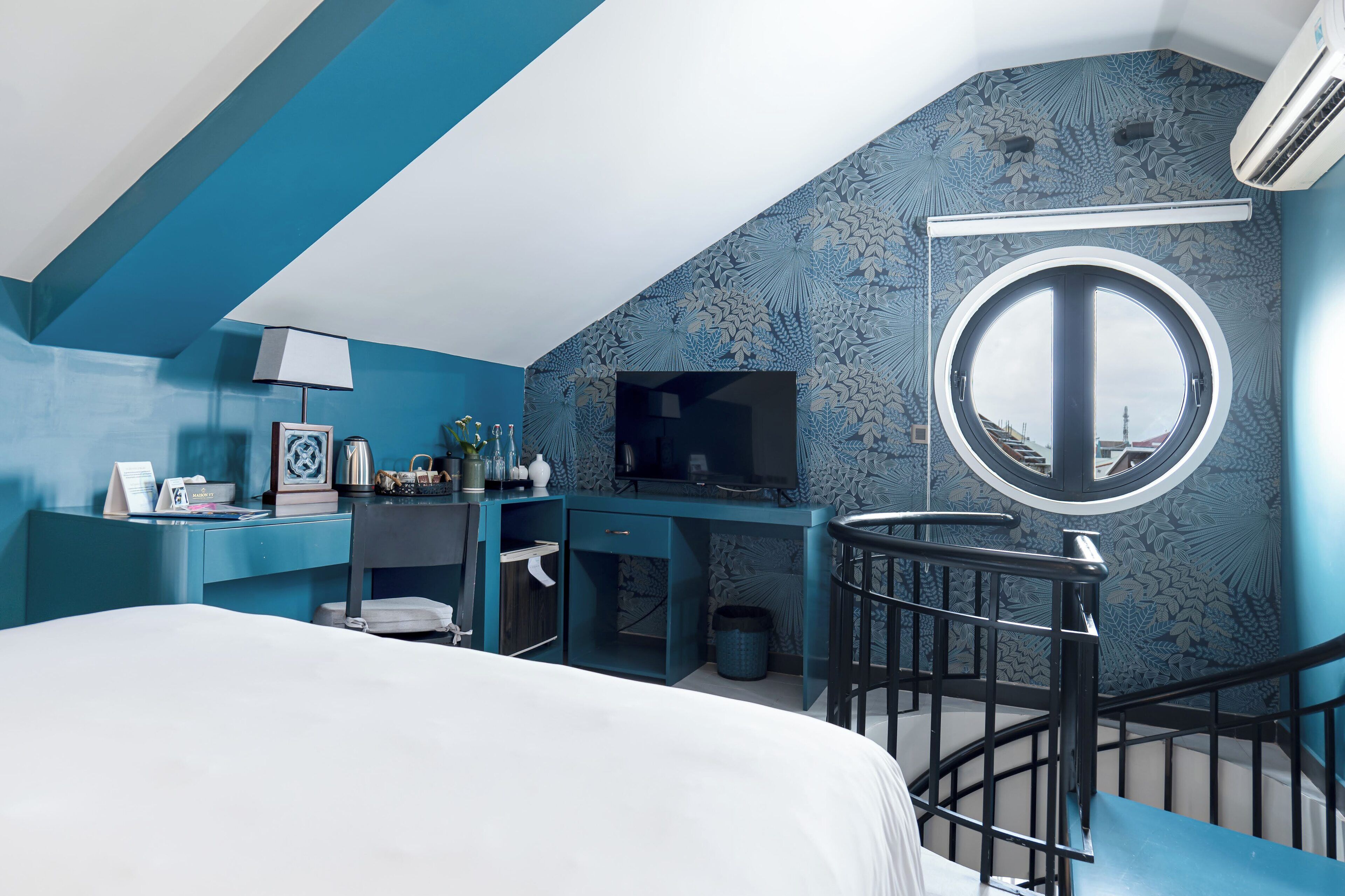 Un dormitorio con cama, escritorio, televisor y una ventana circular.