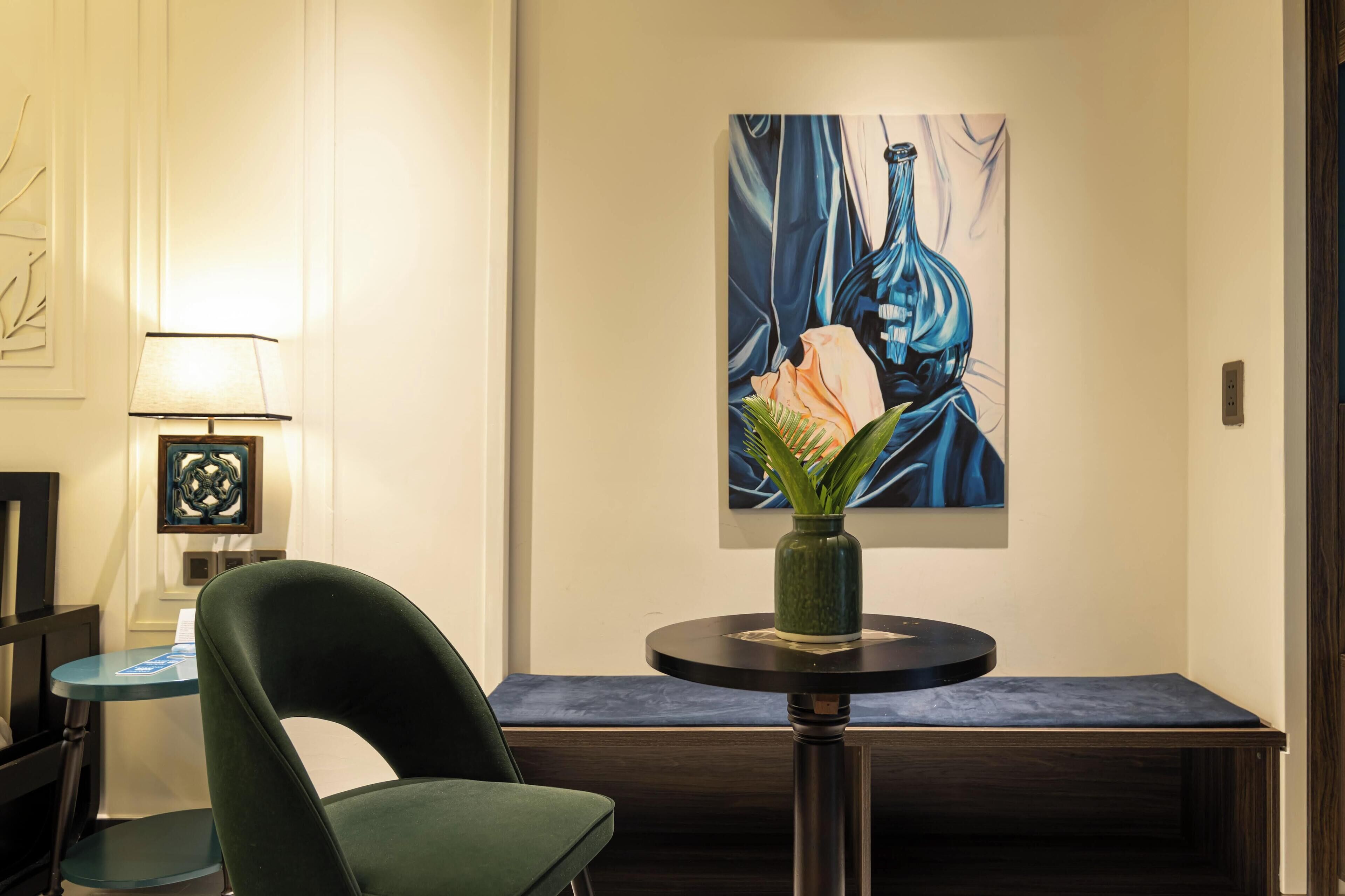 A modern lobby with a green chair, a small round table with a vase, and a large abstract painting on the wall.