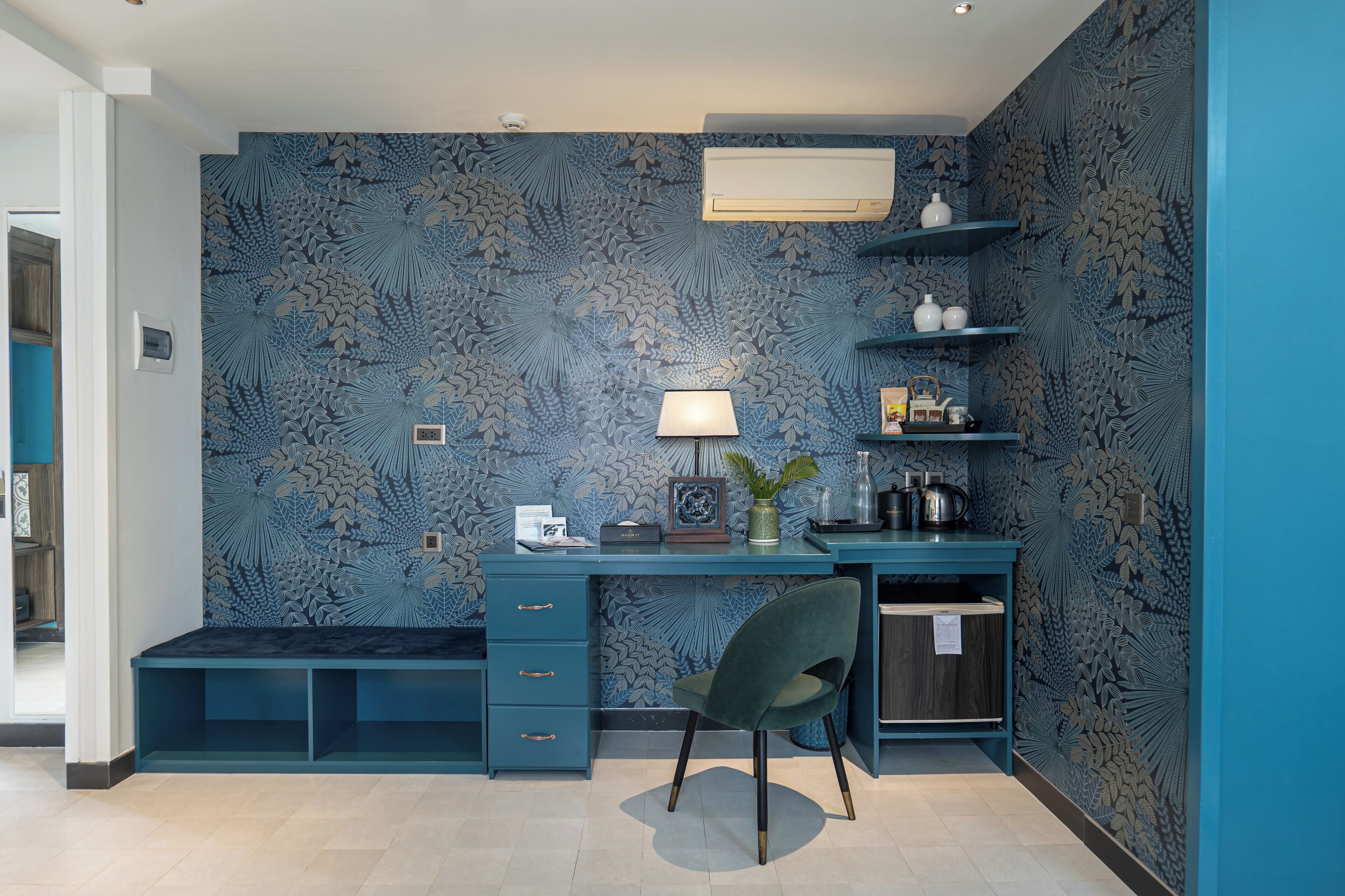 A modern study room with a blue patterned wall, a desk with drawers, a chair, and shelves with decorative items.