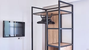 A room with a TV mounted on the wall, a wooden shelf unit with a hanging rack, and a light switch. - Hostel Floridita Adults Only (Calvia)