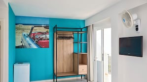 A room with a teal wall, a wooden shelf unit, a white mini-fridge, and a mounted TV. - Hostel Floridita Adults Only (Calvia)
