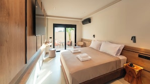 A modern hotel room with a large bed, a flat-screen TV mounted on the wall, a small table with a cup, and a view of the outdoors through a glass door. - Hippocampus Hotel (Rhodes)