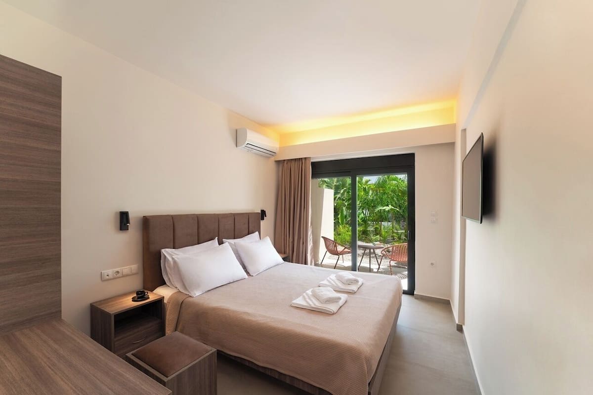 A modern hotel room with a large bed, a nightstand, a TV, and a sliding glass door to an outdoor area.