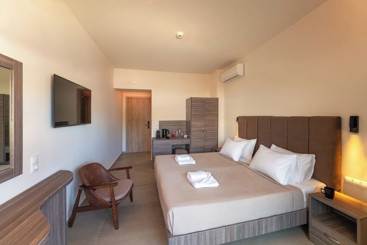 Una habitación de hotel moderna con una cama grande, una mesita de noche de madera, una silla, un escritorio y un televisor montado en la pared.