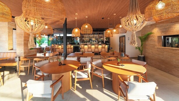 A modern restaurant with wooden furniture, hanging wicker chandeliers, and a bar area in the background. - Hippocampus Hotel (Rhodes)