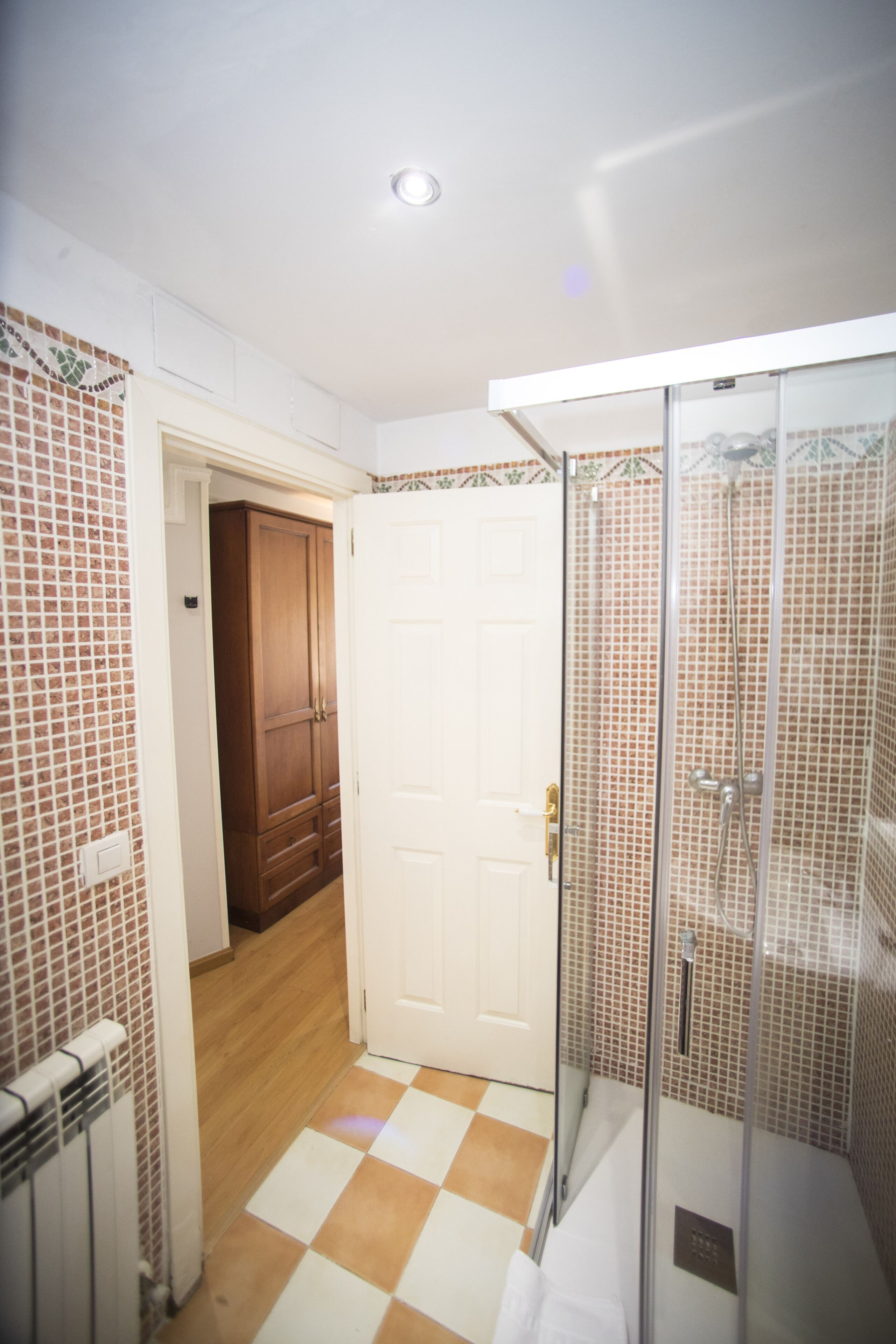 Un baño con ducha, suelo de baldosas y puerta de madera.