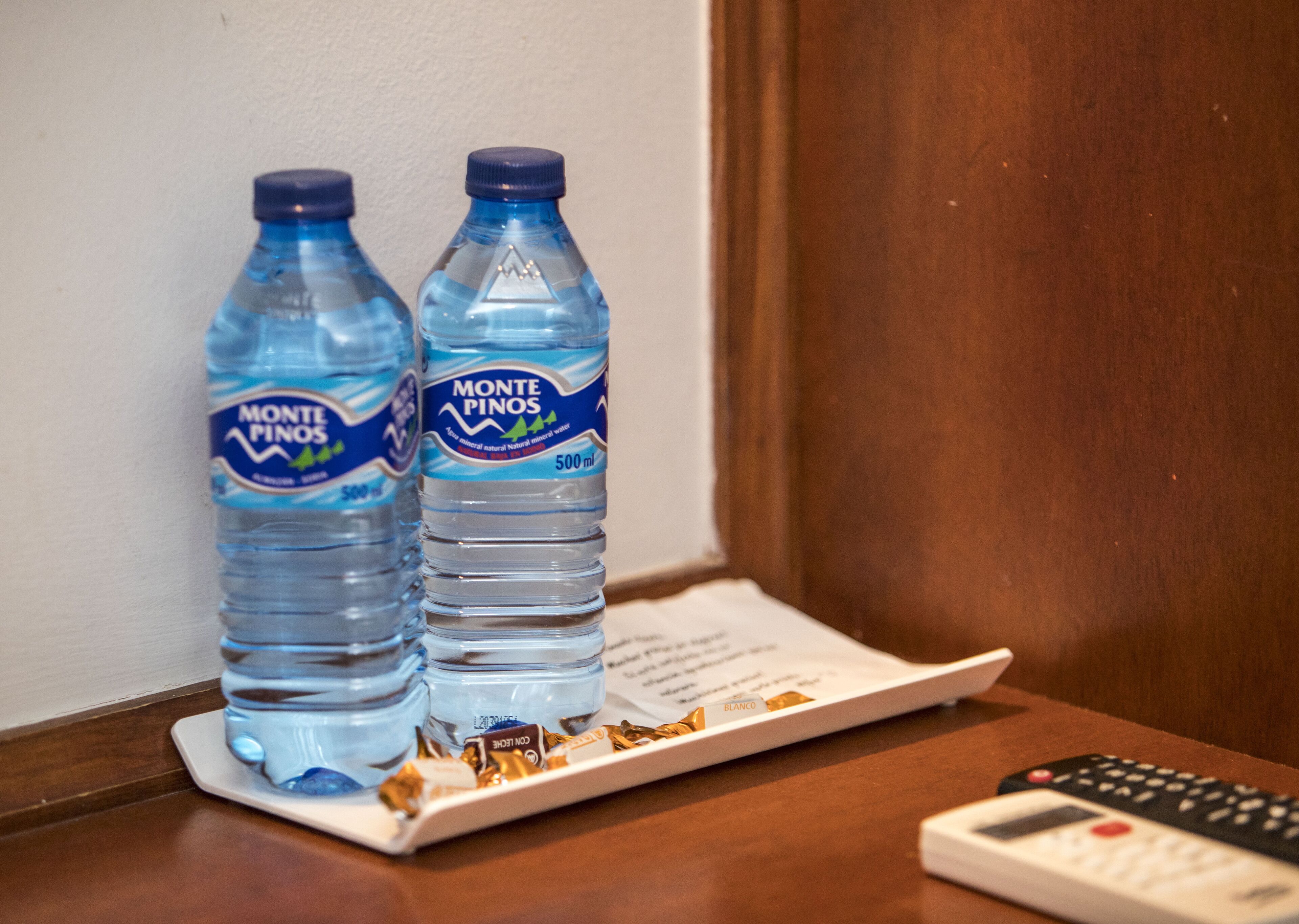 Twee flessen Monte Pinos water op een dienblad, naast een afstandsbediening.