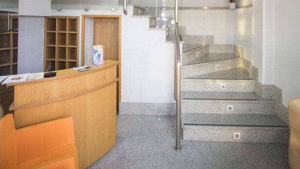 A reception area with a wooden desk, a glass staircase, and a wall-mounted sign. - Hotel Alba (Soria)