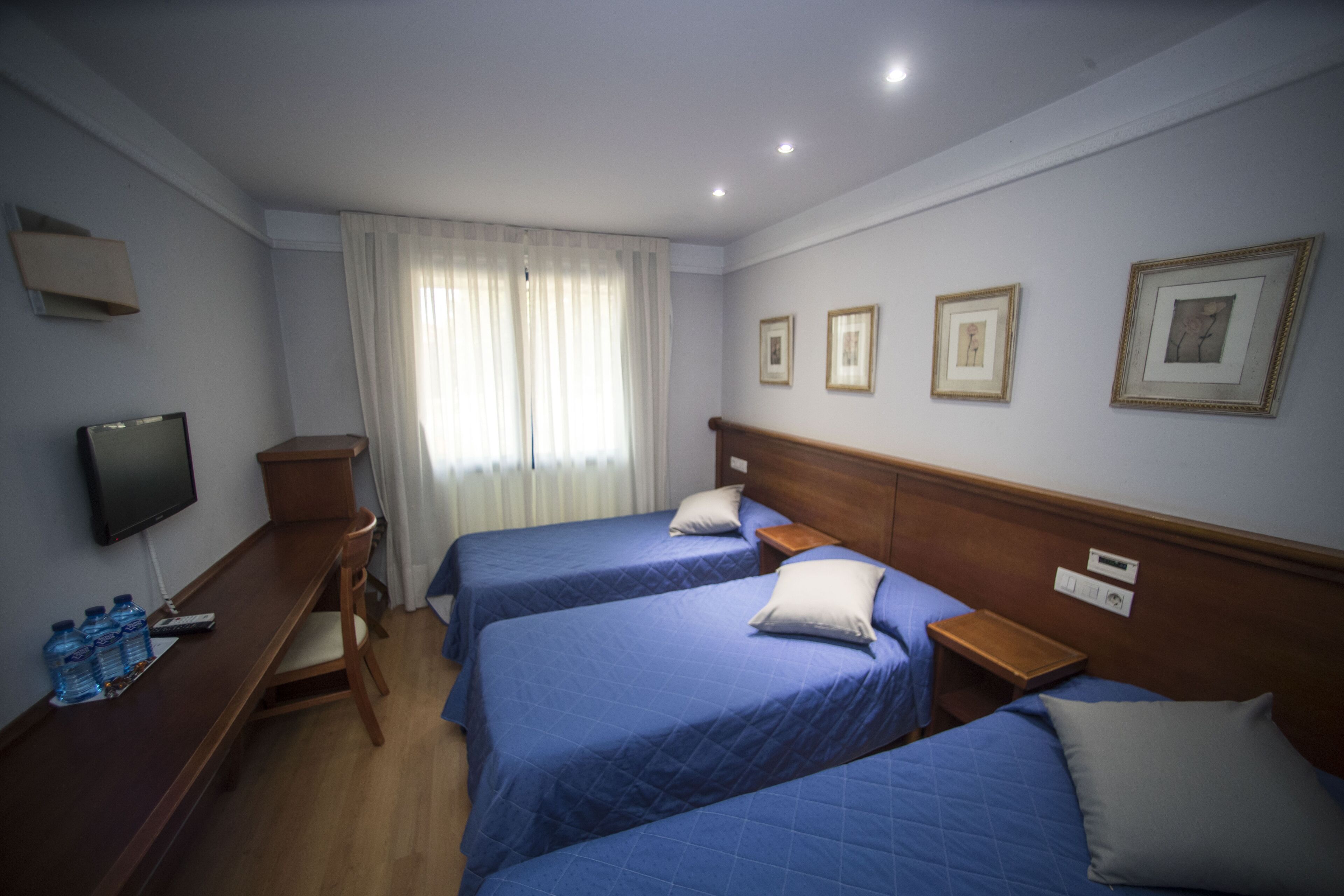 A hotel room with two beds, a TV, a desk with a chair, and a window with curtains.