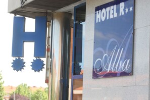 A hotel entrance with a prominent 'H' sign and a sign that reads 'HOTEL R' with a stylized 'R' and 'Alba' written below. - Hotel Alba (Soria)