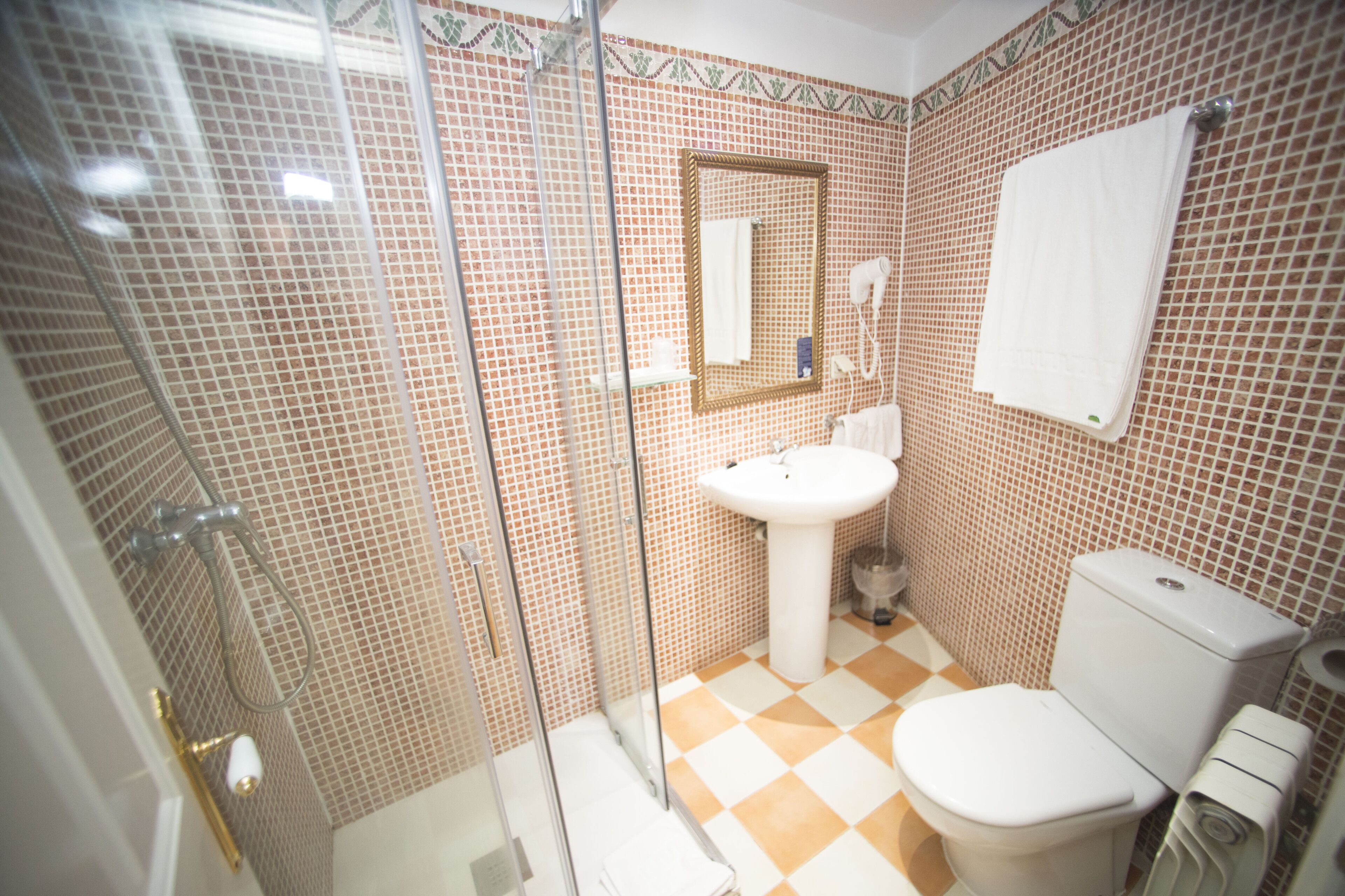 Une salle de bain avec un carrelage à motifs, un lavabo blanc, des toilettes et une douche à parois de verre.