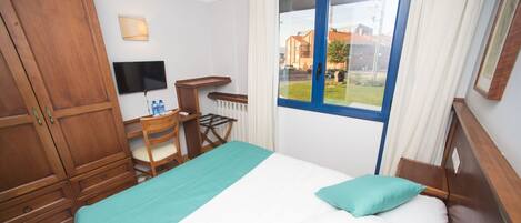 A hotel room with a bed, a desk, a chair, a TV, and a window with a view of buildings.