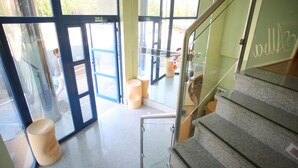 A modern interior with a staircase, glass doors, and a seating area with stools. - Hotel Alba (Soria)