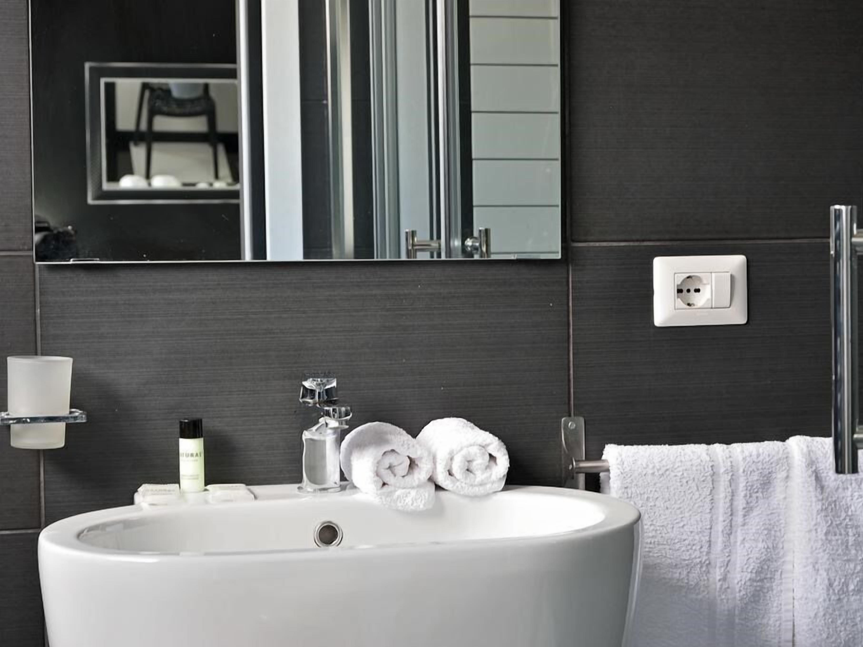 Une salle de bain moderne avec un grand lavabo blanc, un miroir, un porte-serviettes et un flacon de savon liquide.