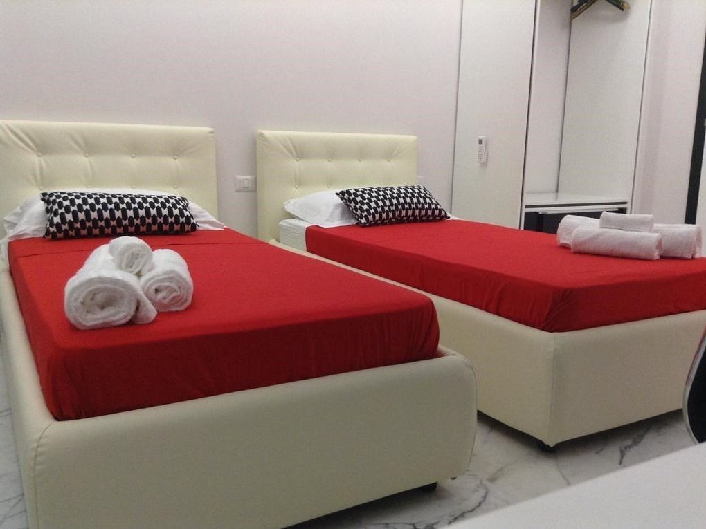 Two twin beds with red and white bedding, white headboards, and a white wardrobe in the background.