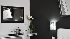 A modern hotel room with a white desk, a chair, a bed with floral bedding, a black wall, and a mirror. - Black & White G&G (Rome)