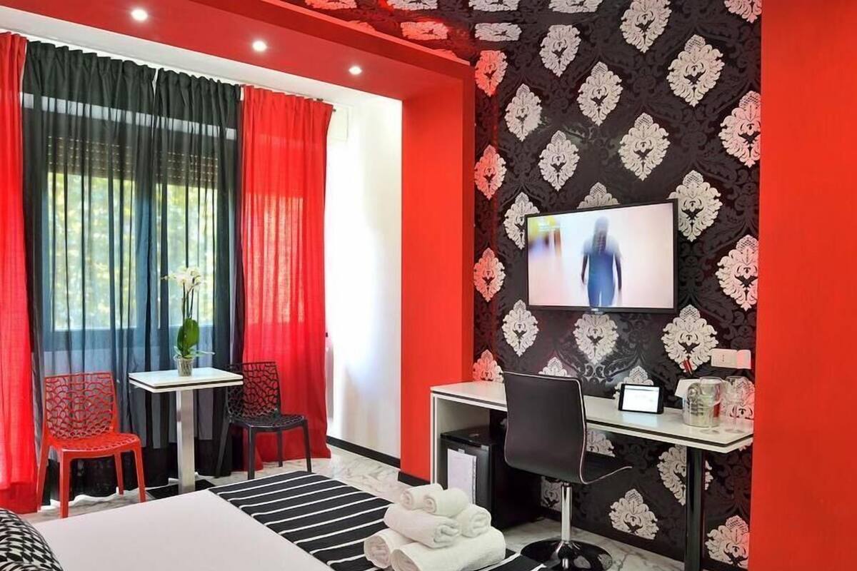 A hotel room with a bed, a desk, a chair, a TV, and a window with curtains.