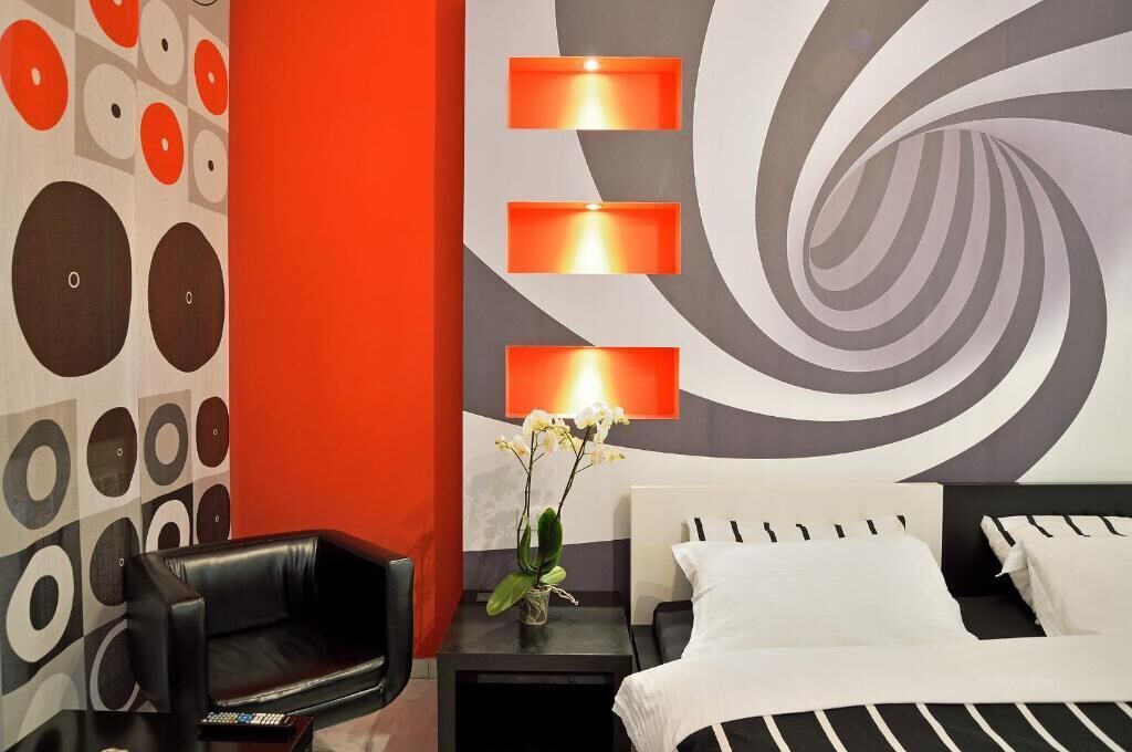 Una habitación de hotel moderna con un sofá de cuero negro, una cama con ropa de cama blanca y una pared con un diseño circular y un gran motivo espiral.