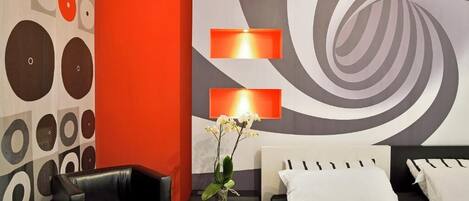 Una habitación de hotel moderna con un sofá de cuero negro, una cama con ropa de cama blanca y una pared con un diseño circular y un gran motivo espiral.