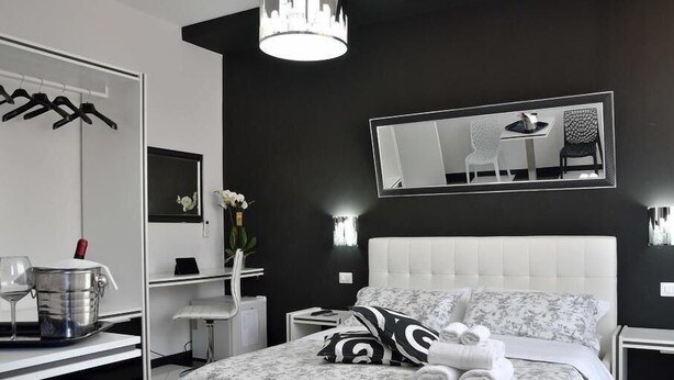 A modern bedroom with a large bed, a bedside table, a chair, a mirror, and a hanging light fixture. - Black & White G&G (Rome)