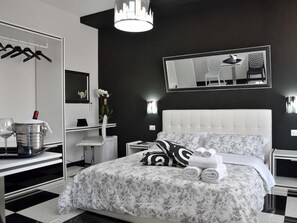 Et moderne soveværelse med en stor seng, et natbord, en stol, et spejl og en hængende lampe.