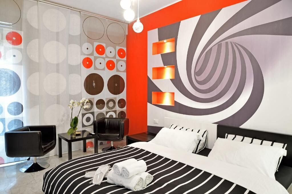 Een moderne hotelkamer met een groot bed, een flatscreen televisie, een zithoek met een fauteuil, en een wand met ronde patronen.