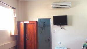 Een badkamer met een houten deur, een grijze douchecabine, een bevestigde televisie en een airconditioning op de muur.