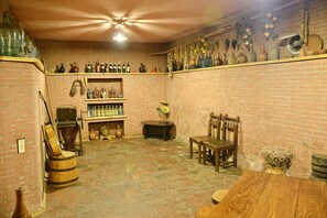 Una bodega rústica con paredes de ladrillo, barriles de madera y estantes llenos de botellas y cerámica.