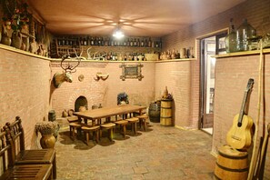 Una habitación rústica con pared de ladrillo, muebles de madera y diversos objetos decorativos, incluyendo una cabeza de venado, una guitarra y una colección de botellas.