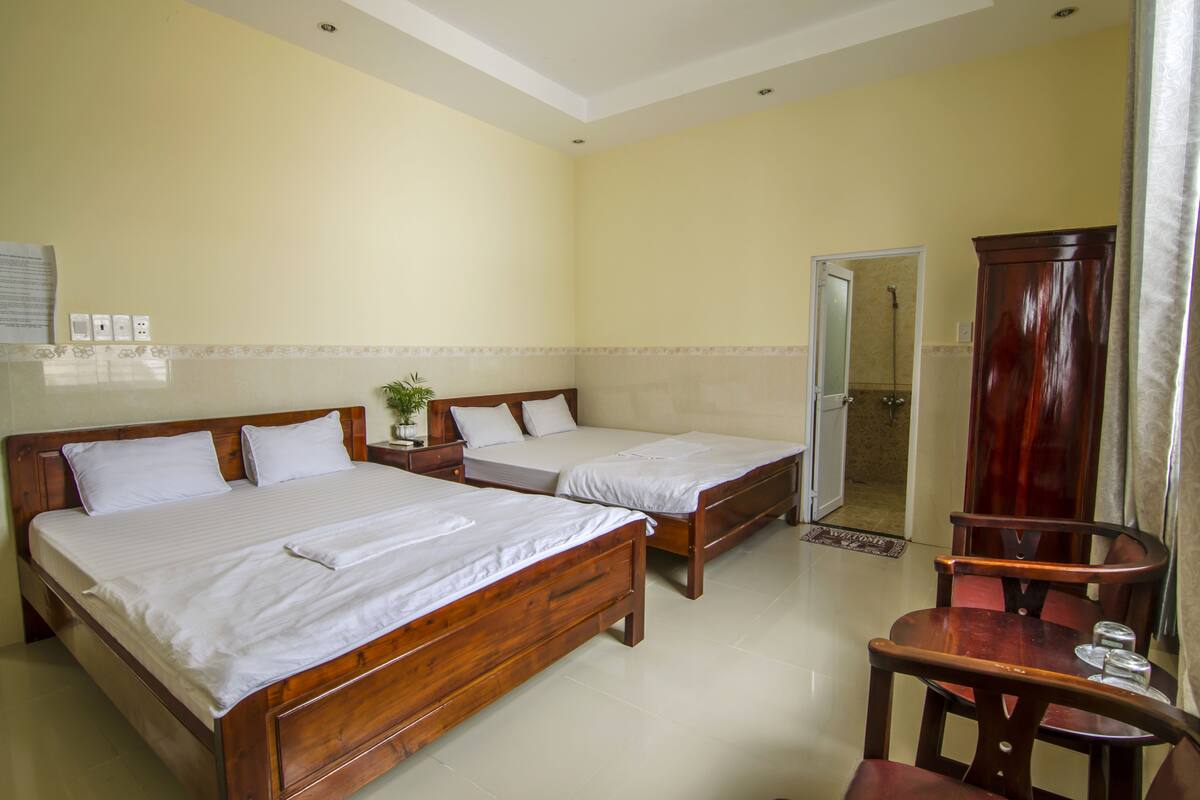 A hotel room with two wooden beds, a wooden chair, a small table, and a mirror.
