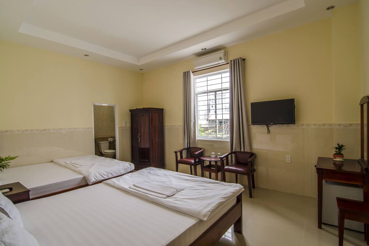 A hotel room with two beds, a TV, a desk, and a window with curtains.