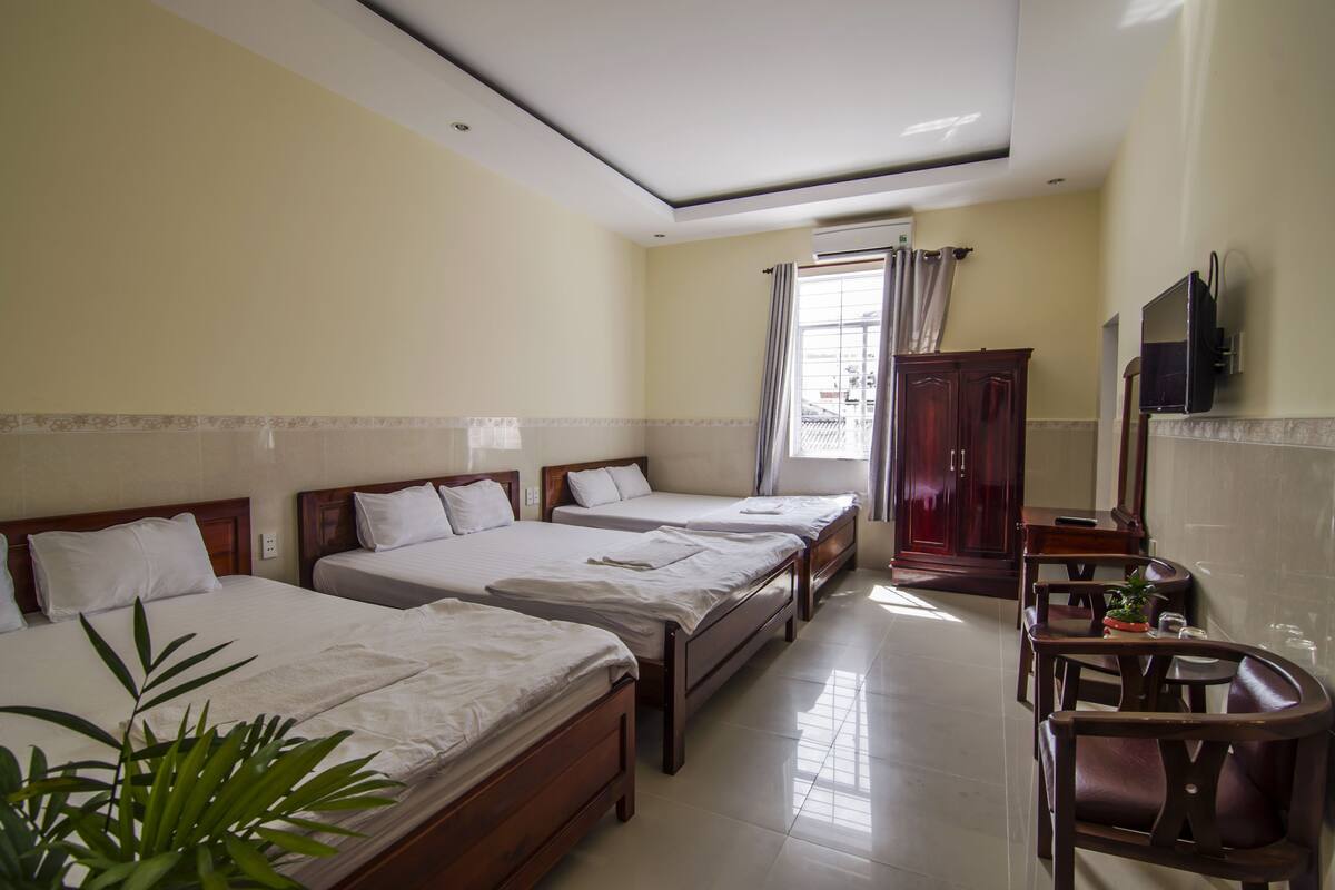 A hotel room with three single beds, a wooden cabinet, a television, and a small table with chairs.