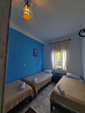 A room with two beds, a window with curtains, a wall clock, and a decorative light fixture. - Hostal La Joya (Chefchaouen)
