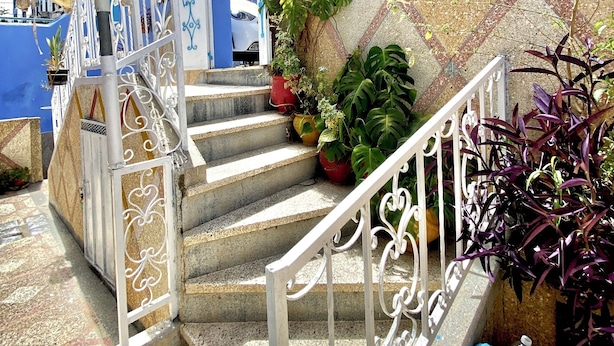 Eine Treppe mit weißen Geländern, die zu einem Gebäude mit blauen und beigen Wänden führt.