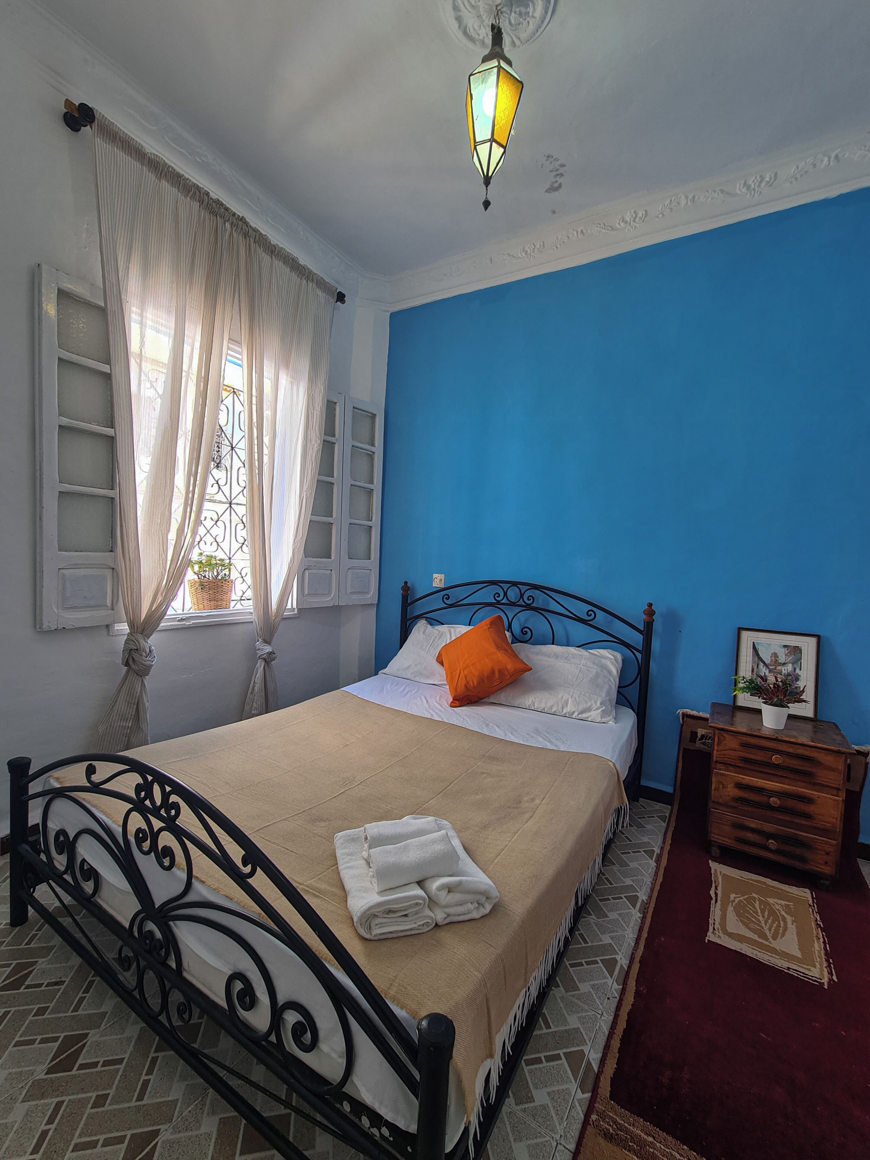 A bedroom with a bed, a nightstand, a lamp, a window with curtains, and a blue wall.