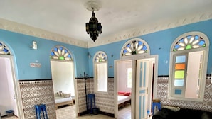 Ein Zimmer mit Fliesenboden, einer schwarzen Couch, einem Bett mit gemustertem Kopfteil und einer blauen Wand mit dekorativen Bögen.