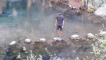 A person standing on rocks in a clear water body surrounded by rocky terrain and sparse vegetation.