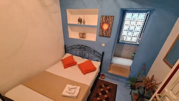 Un dormitorio con cama, almohadas, un estante con adornos, una ventana y una puerta.