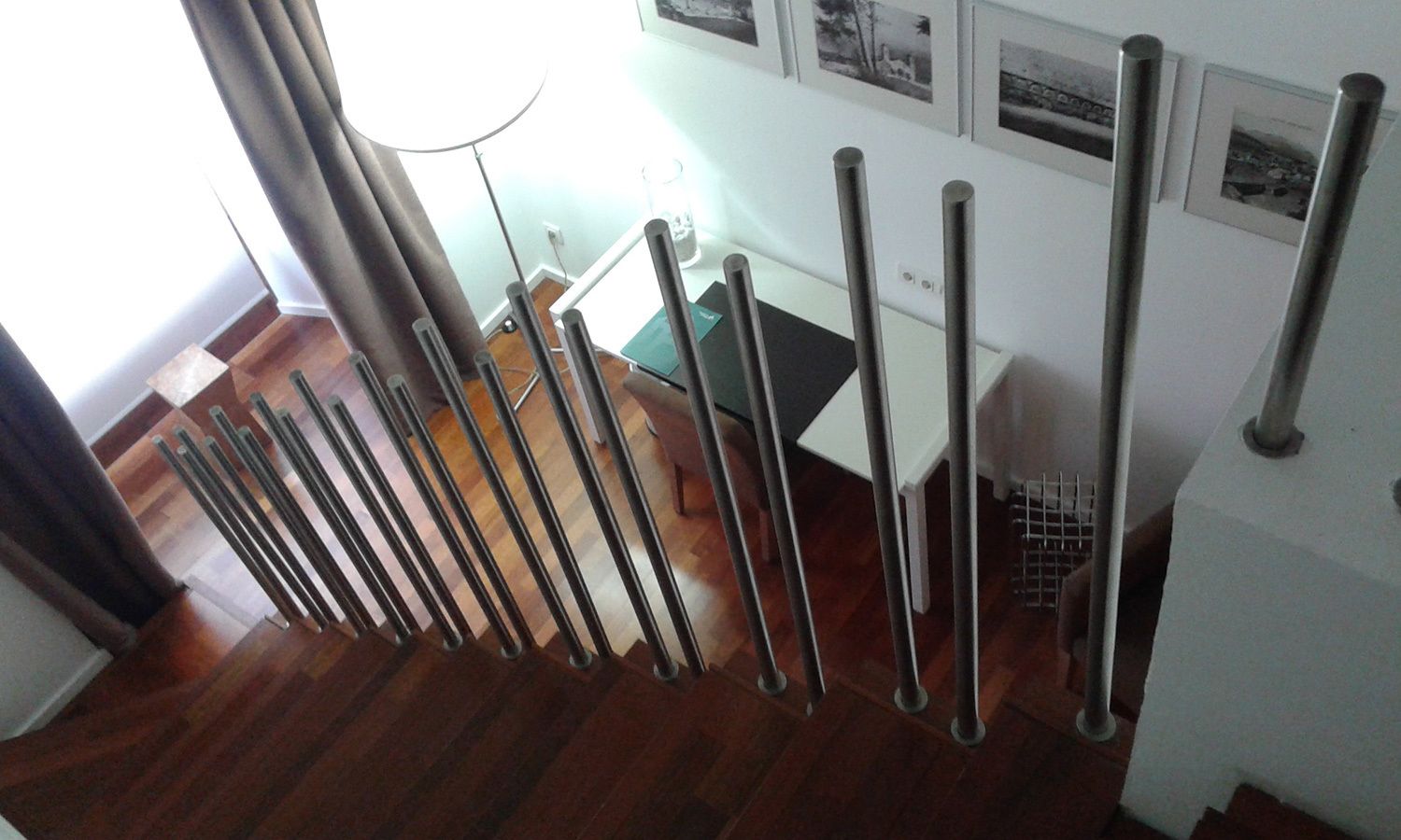Una escalera con barandillas de metal, suelo de madera y una pared blanca con cuadros enmarcados.