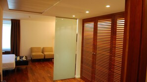 A hotel room with a bed, a sofa, a desk, and a sliding door with wooden blinds.